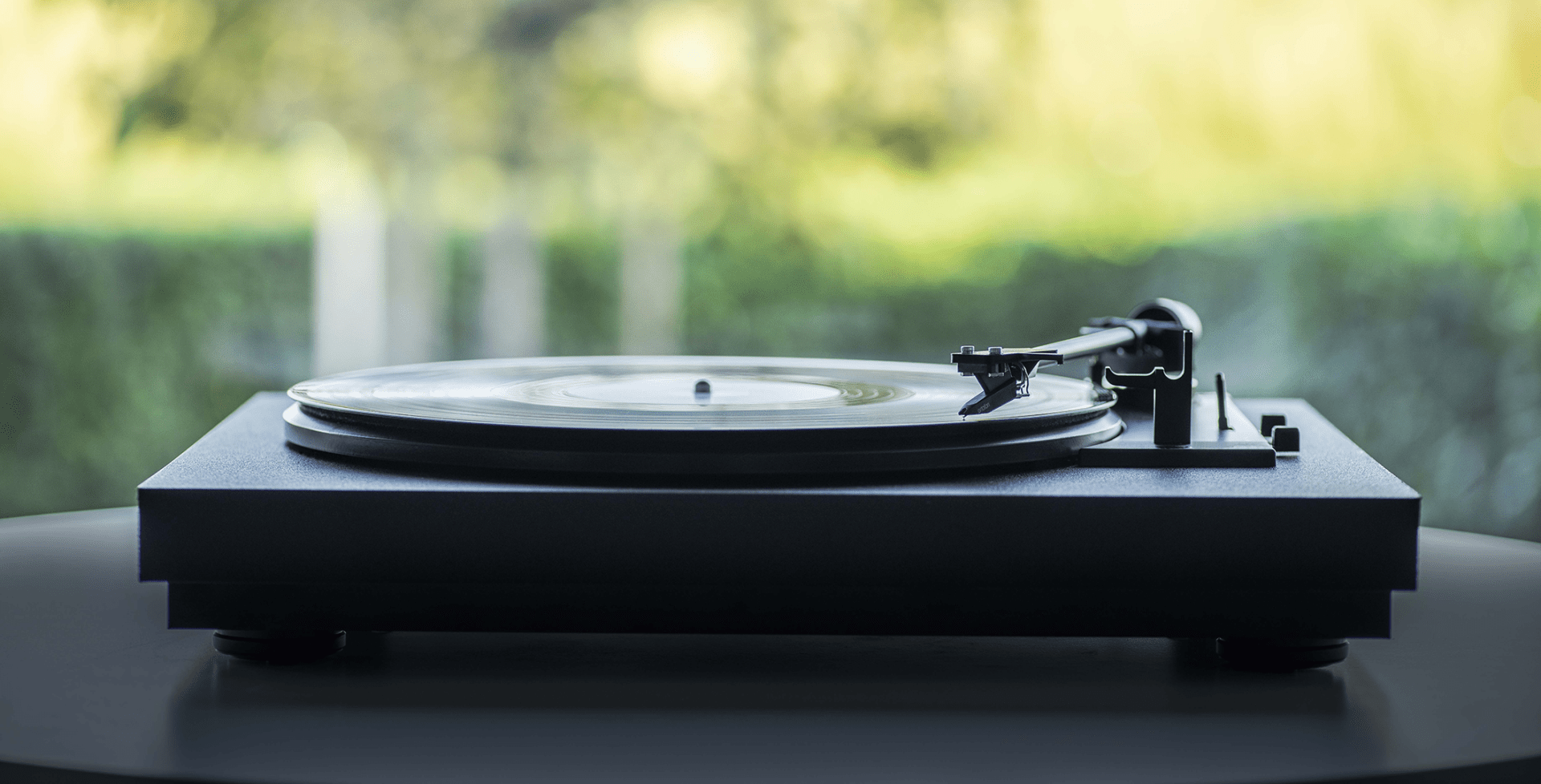 Ein schwarzer Plattenspieler mit einer Vinyl-Schallplatte darauf. Ein verschwommener Hintergrund mit grünem Laub.