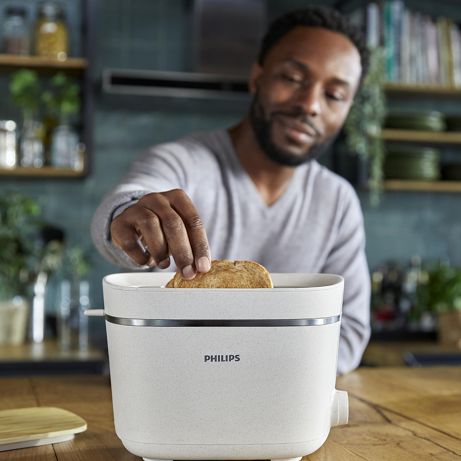 Uomo che prende pane tostato da un tostapane bianco, logo Philips visibile.