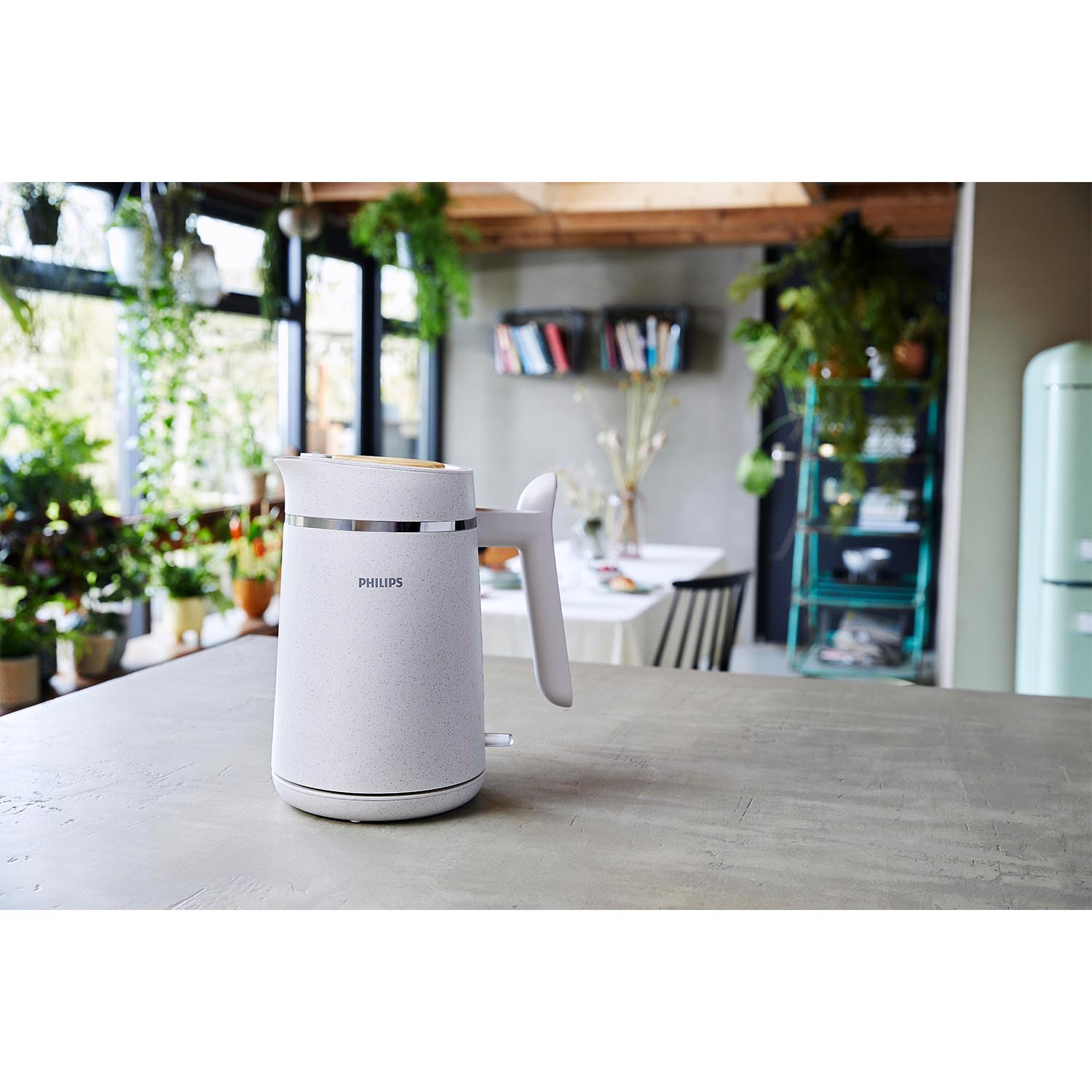Bollitore Philips bianco sul piano di lavoro. Cucina con piante e zona pranzo sullo sfondo.