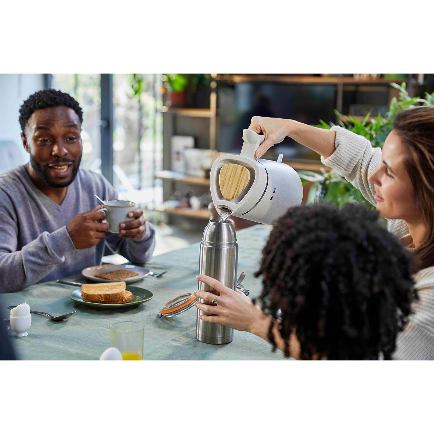 Persone che fanno colazione; qualcuno versa acqua in un thermos da un contenitore bianco.