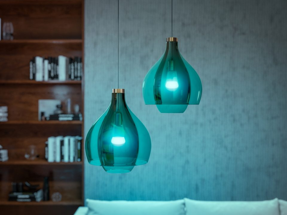 Deux lampes suspendues turquoise sont suspendues devant un mur gris et une bibliothèque.