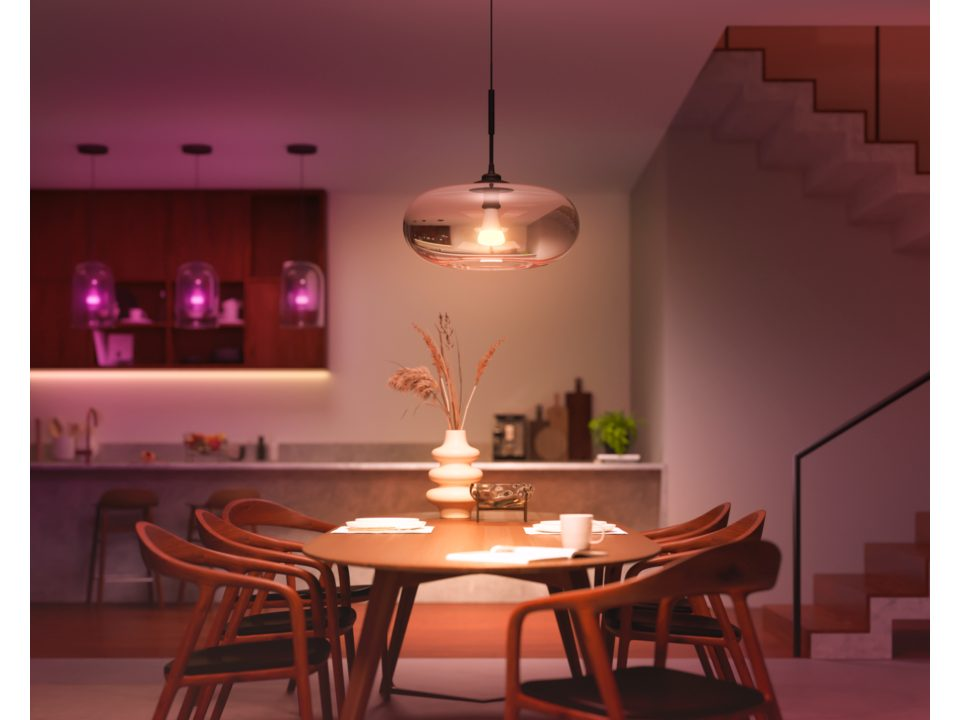 Une salle à manger avec une table et des chaises, une lampe suspendue et une cuisine en arrière-plan.