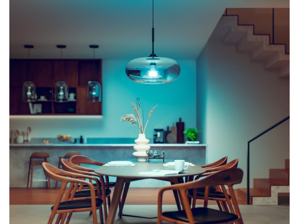 Une salle à manger avec une table ronde, des chaises et un luminaire suspendu bleu. Les murs sont sombres.