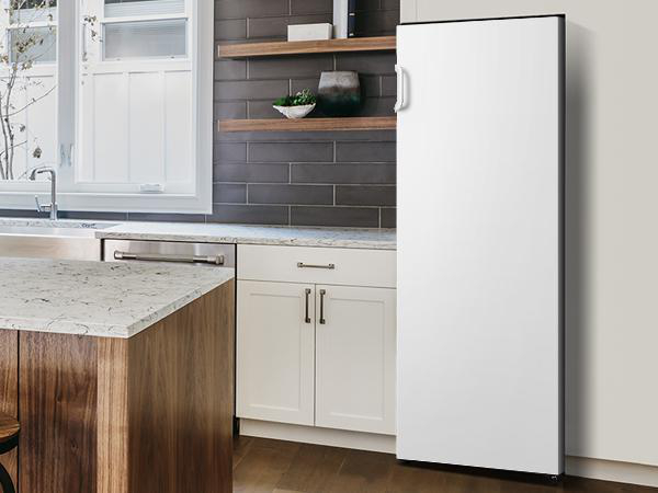 Weißer Kühlschrank in der Küche. Graue Ziegelmauer und Holzinsel im Hintergrund.