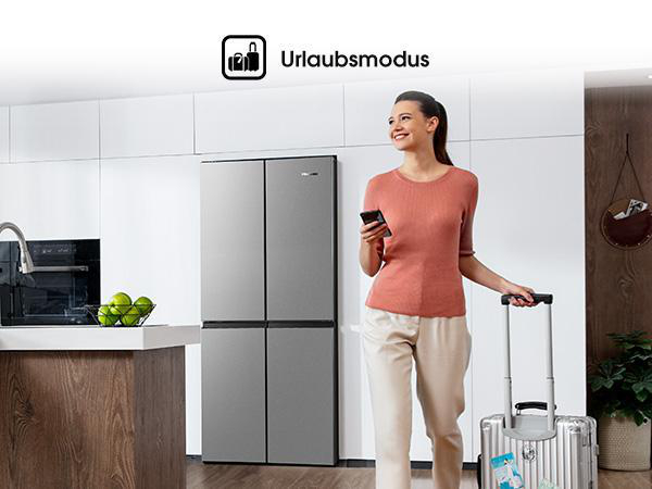 Eine Frau in einem Raum mit Kühlschrank und Gepäck, darüber der Text 'Urlaubsmodus'.