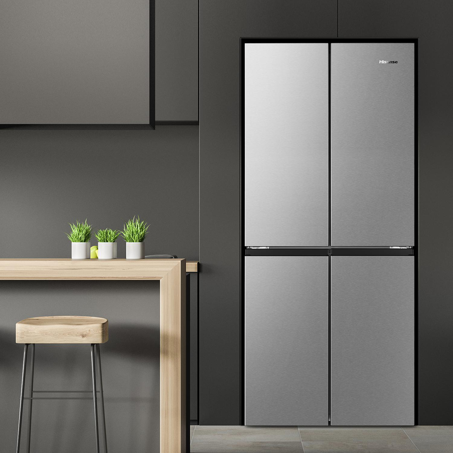 Edelstahl-Hisense-Kühlschrank mit vier Türen. Ein Holztisch mit Pflanzen und ein Hocker befinden sich im Vordergrund.