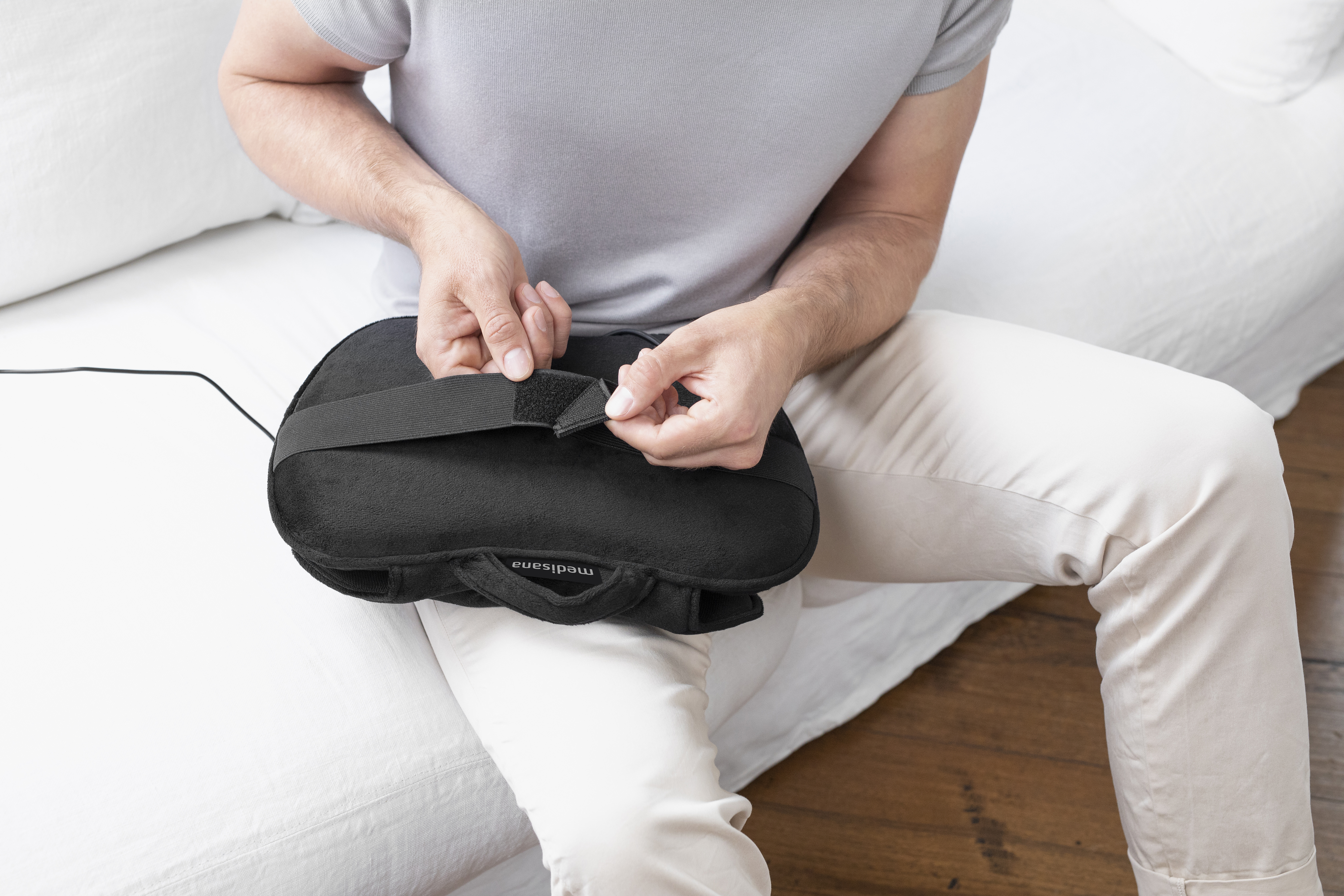 Un homme assis sur un lit, attachant une sangle velcro à un coussin de massage noir.