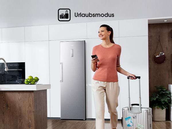 Frau in Küche mit Koffer, Telefon. Kühlschrank links, Text: Urlaubsmode.