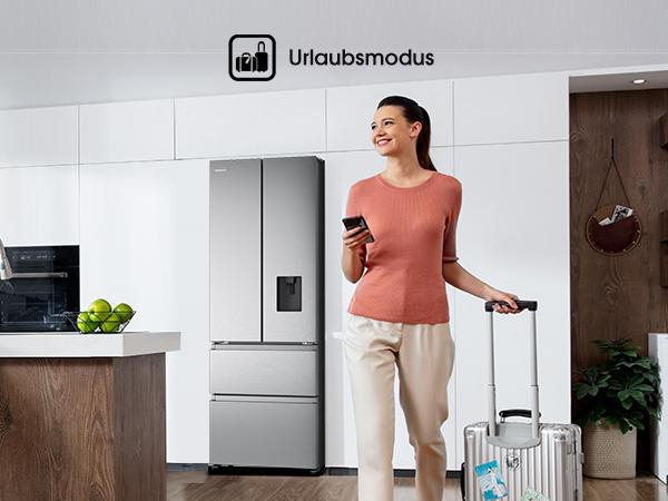 Frau mit Koffer und Telefon in der Küche. Kühlschrank, Obst und Dekorationen sind ebenfalls im Hintergrund zu sehen.