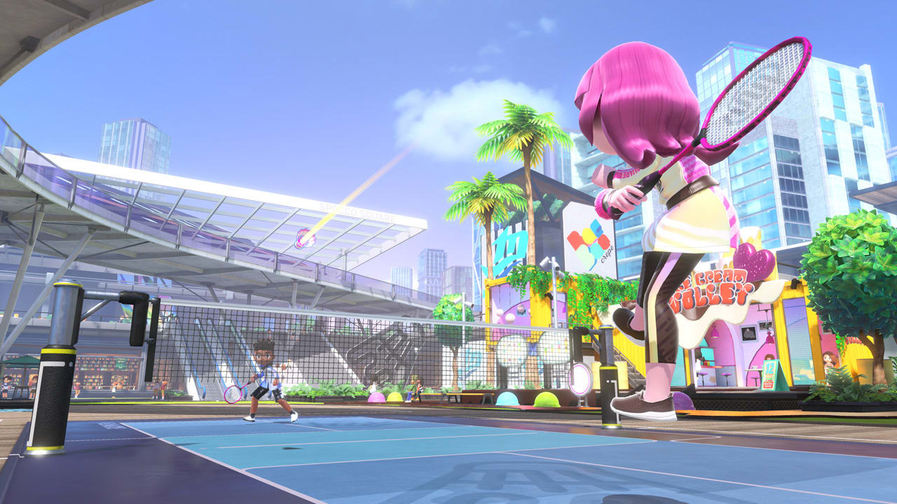 Un gioco di tennis a cartoni animati. Due giocatori colpiscono una palla. Lo sfondo è una città.