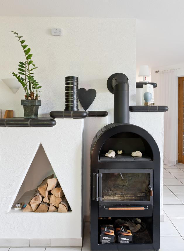 Kamin mit Brennholz, einem schwarzen Ofen und Dekoration. Eine Pflanze und eine herzförmige Dekoration auf dem Regal.