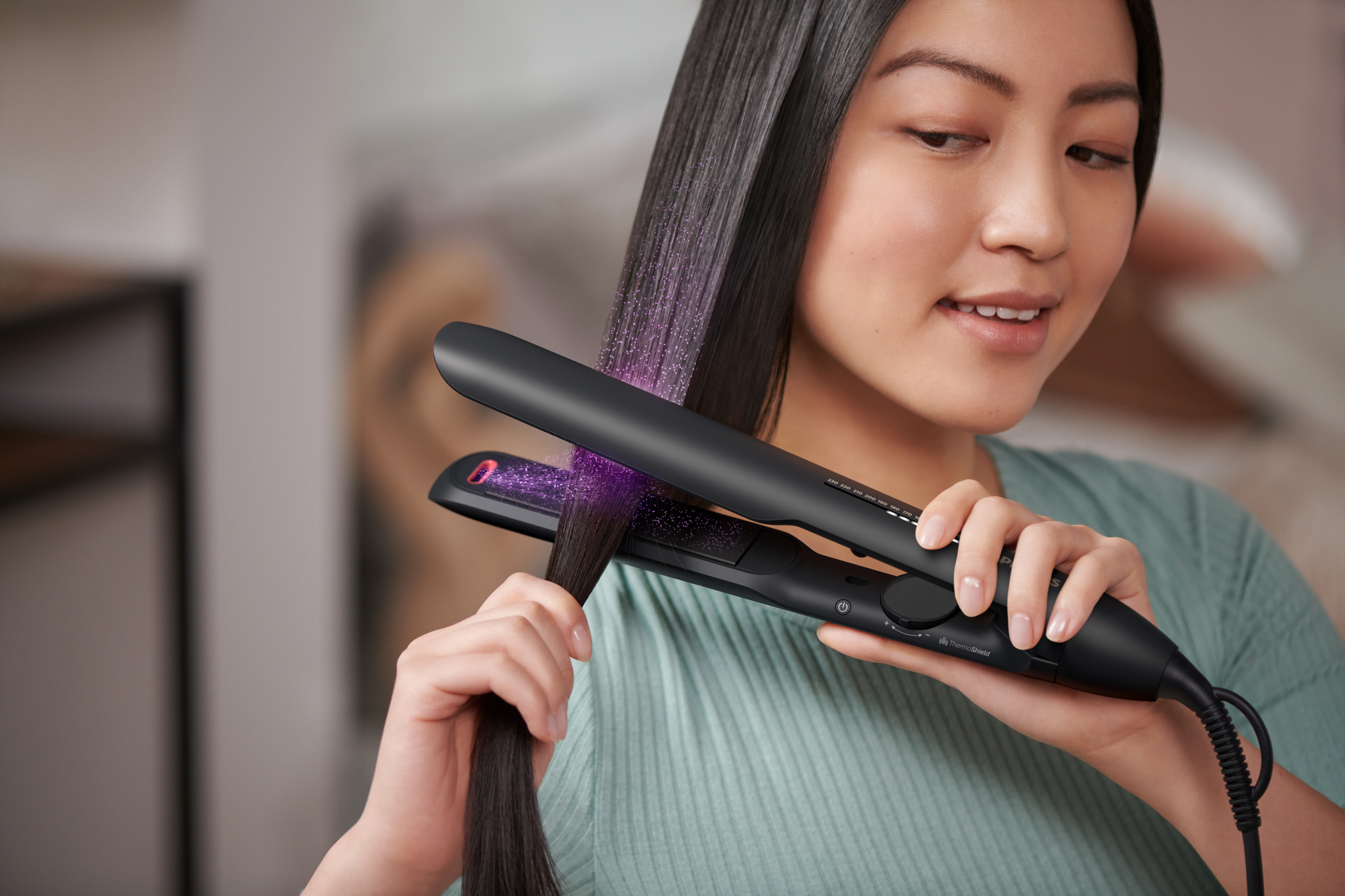 Frau benutzt einen schwarzen Haarglätter. Das Haar ist glänzend und glatt. Der Glätter ist im Haar.