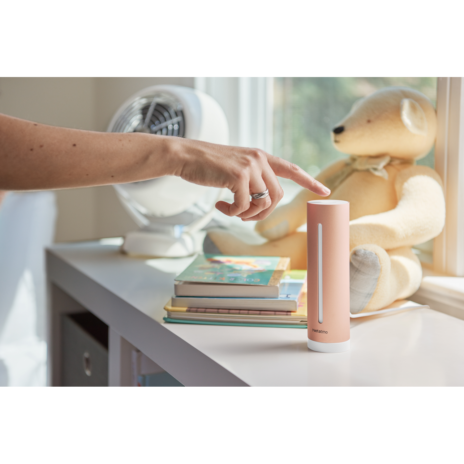La mano de una mujer tocando un monitor de calidad del aire interior inteligente Netatmo rosa.