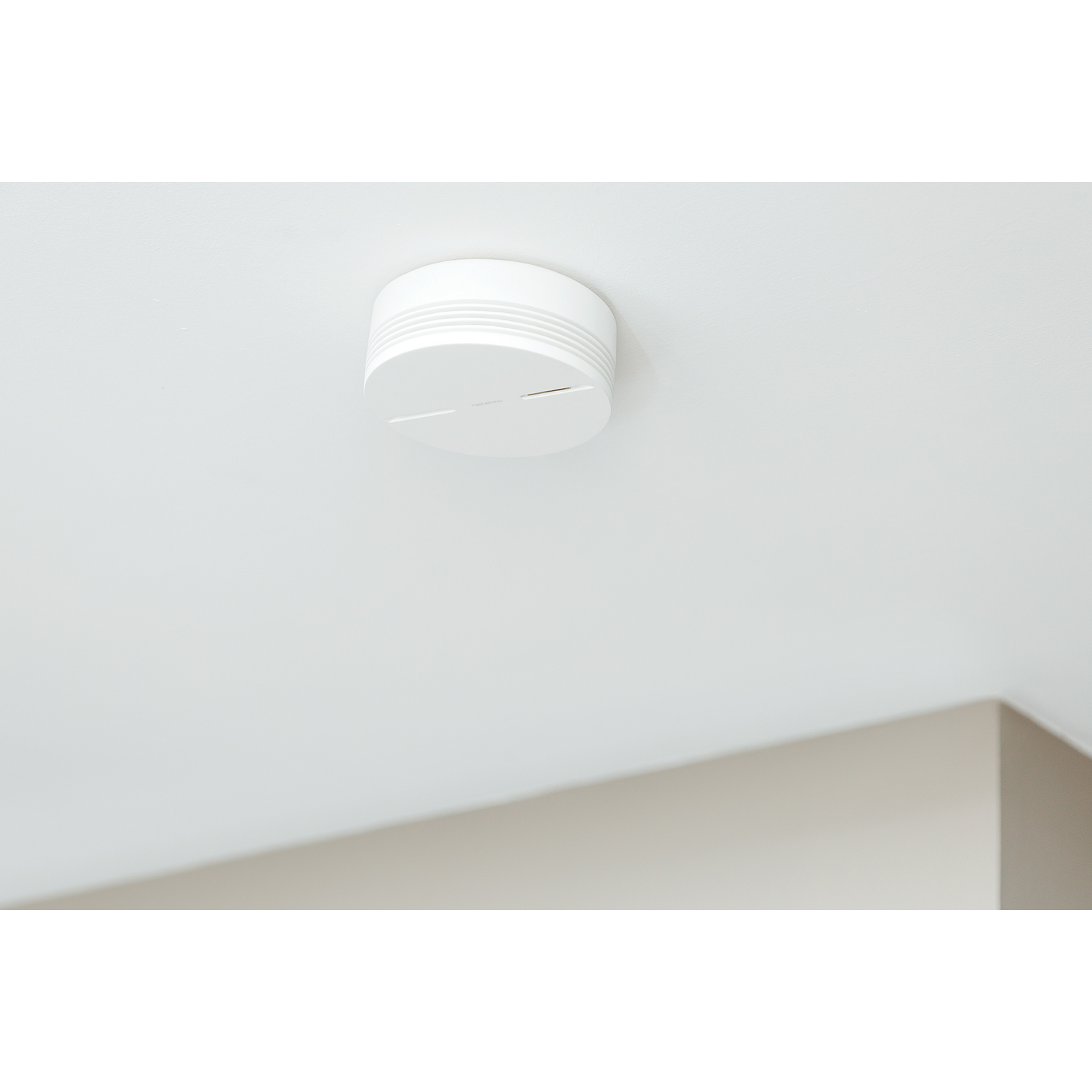 Un detector de humo blanco montado en un techo blanco con una esquina gris.