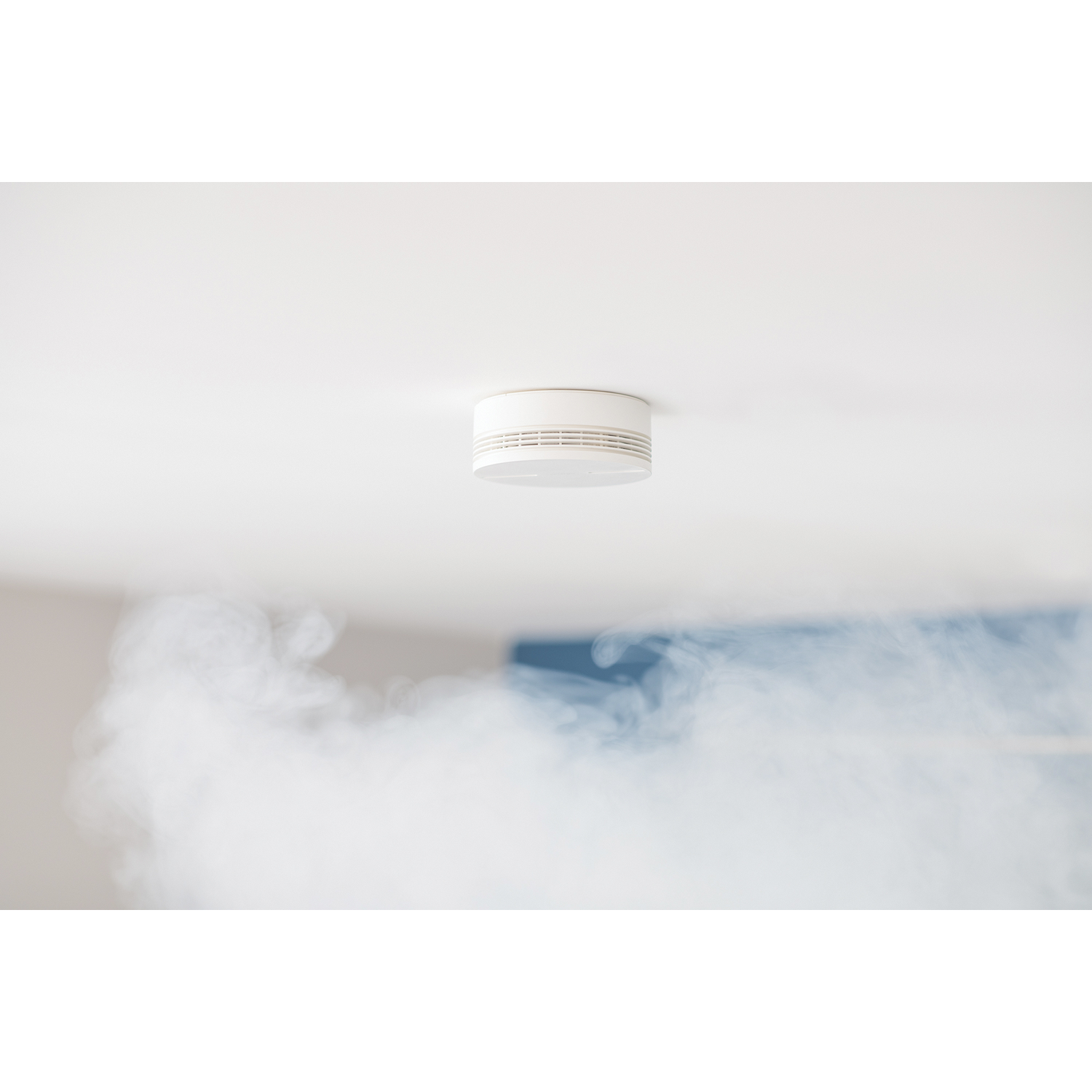 Un detector de humo blanco en un techo. El humo se eleva debajo del detector.