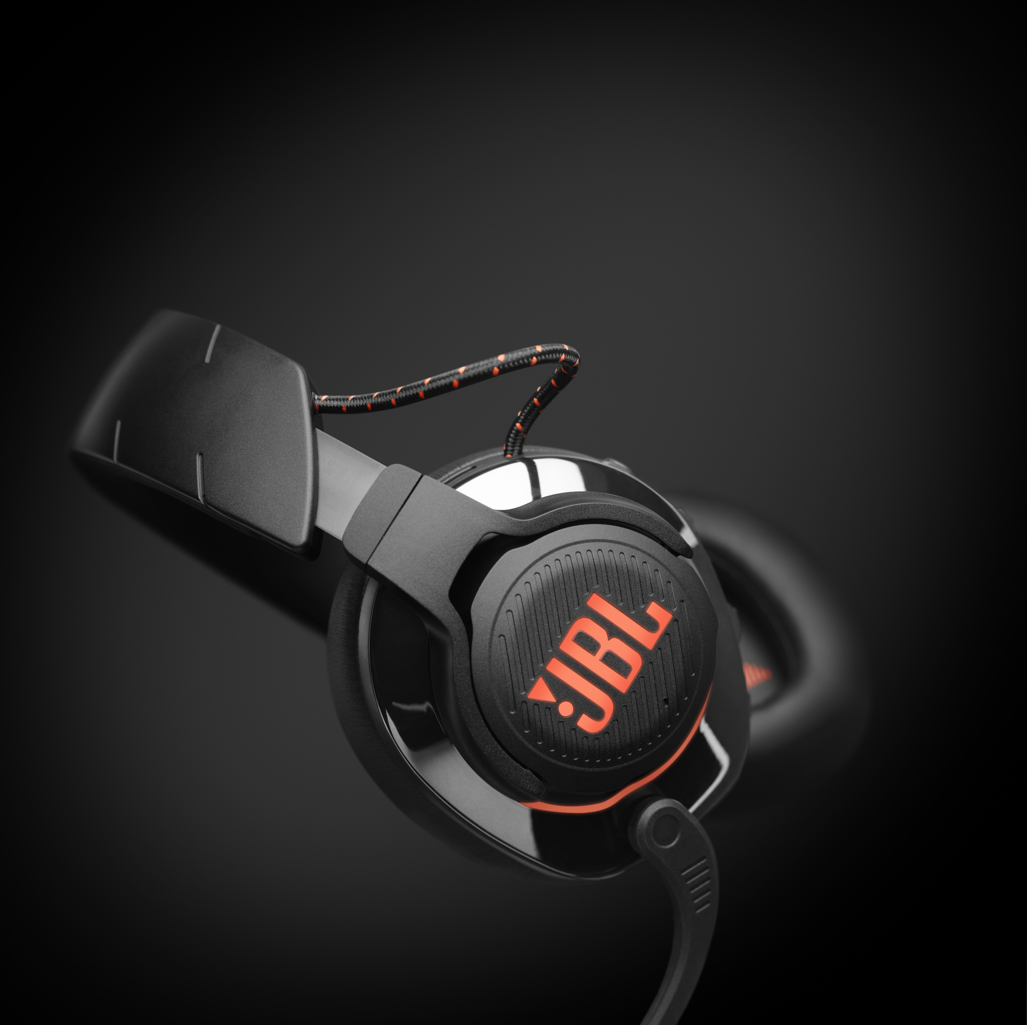Schwarze JBL-Kopfhörer mit dem Markennamen in Orange auf der Ohrmuschel, auf dunklem Hintergrund.