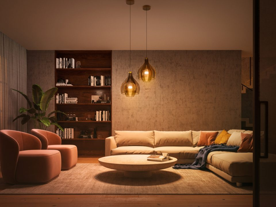 Salon avec canapé, chaises, bibliothèques et suspensions ; éclairage chaleureux.