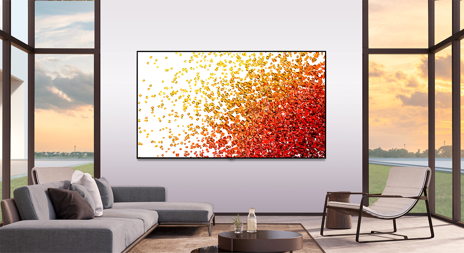 Grote tv toont abstracte kunst op witte muur. Grijze bank, stoel en ramen op de achtergrond.