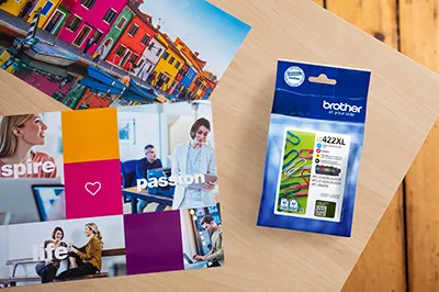 Schreibtisch mit bunten Bildern, Dokumenten und einer Brother-Tintenpatronenbox. Inspirierende Szene.