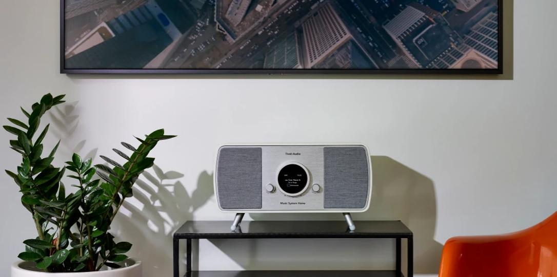 Una radio moderna su un tavolo nero, con una pianta verde a sinistra e un dipinto di paesaggio urbano sopra.