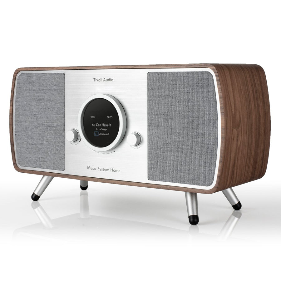 Un sistema musicale Tivoli Audio con fianchi in legno, coperture per altoparlanti grigie e un display centrale. Ha gambe argentate e superficie lucida.