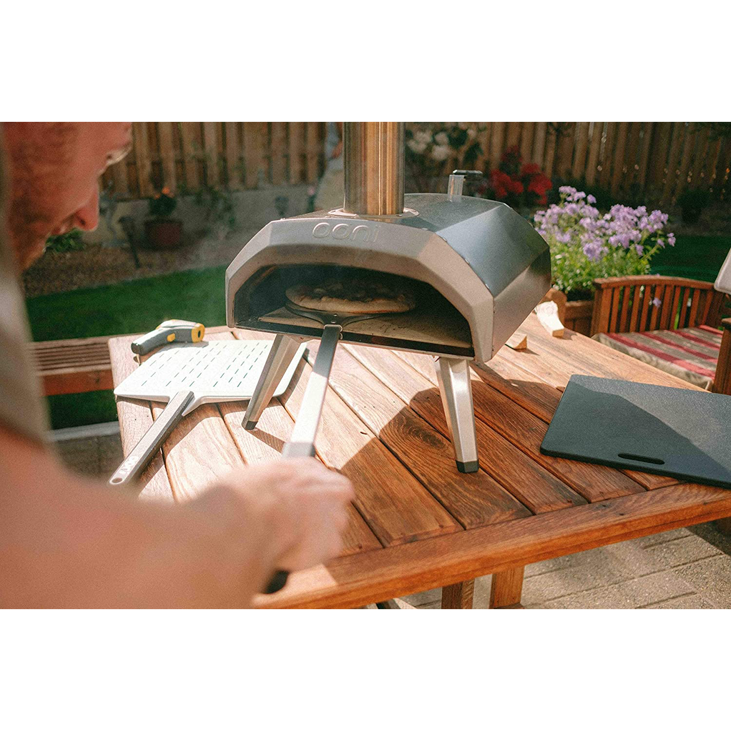 Una persona usa un forno per pizza su un tavolo di legno all'aperto, con pizza all'interno.