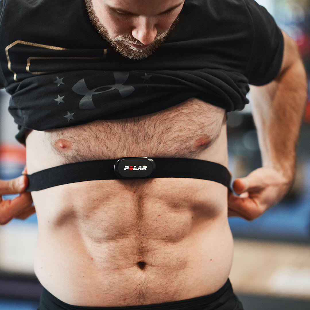 Ein Mann legt einen Brustgurt-Herzfrequenzmesser an. Er befindet sich in einem Fitnessstudio.