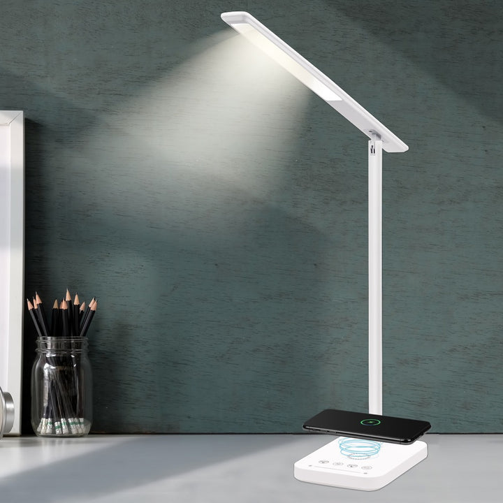 White desk lamp with a charging pad, and a phone on the pad.