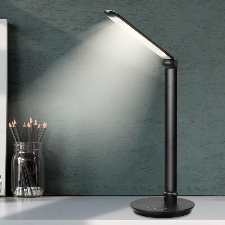 A black desk lamp illuminates a desk. Pencils in a jar are to the left. The background is a textured, teal wall.