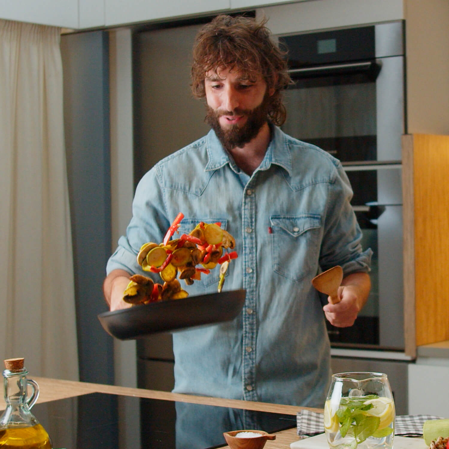 Hombre lanzando comida de la sartén. Ambiente de cocina con aceite y bebida.