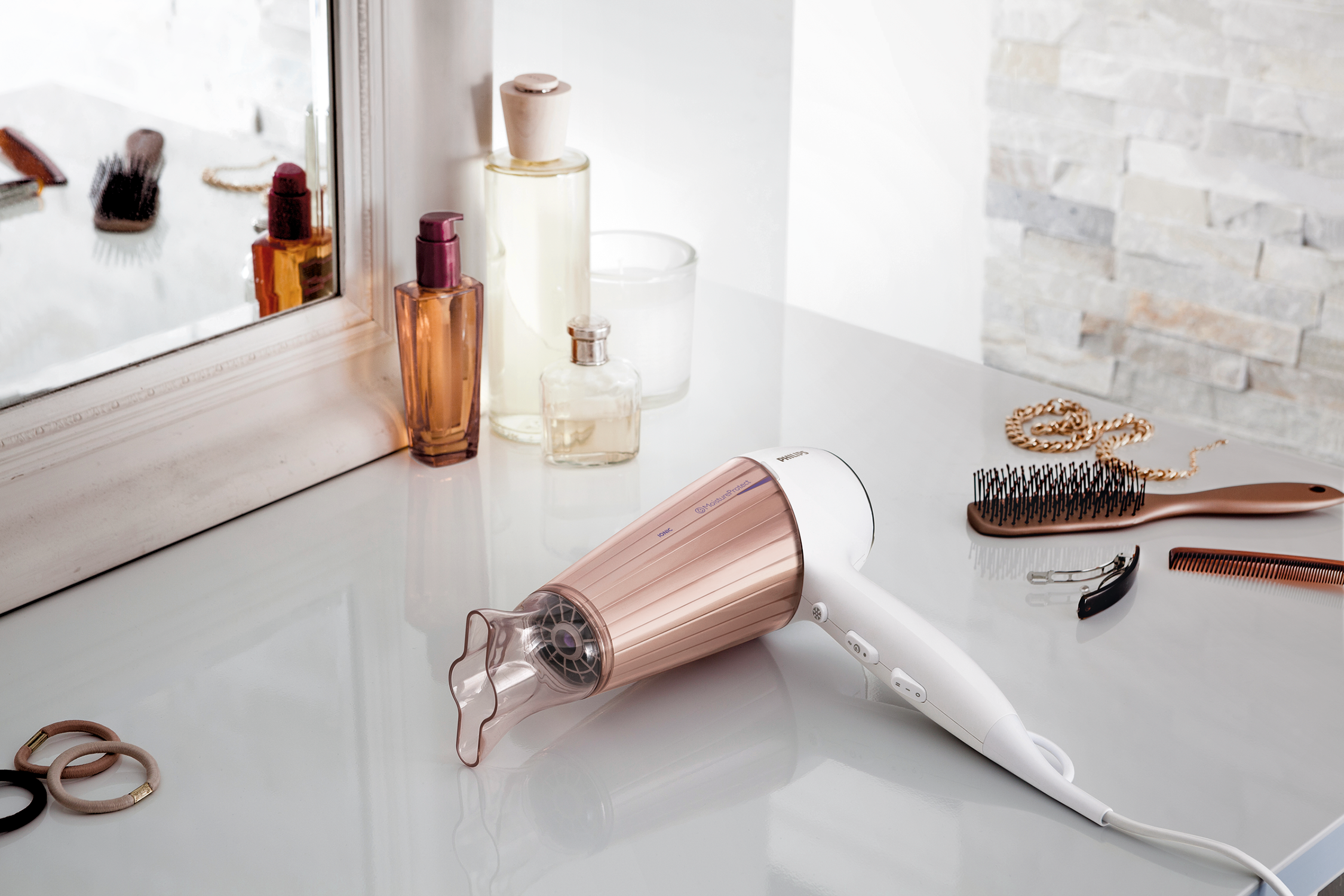 White hairdryer with rose gold accents on a white table with accessories and a mirror.