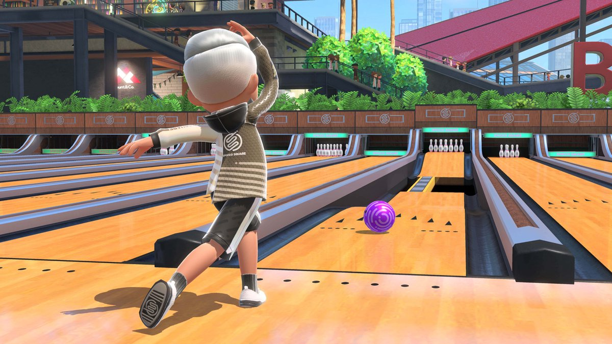Een persoon die aan het bowlen is, op het punt staat een paarse bowlingbal los te laten. Houten baan, kegels op de achtergrond.