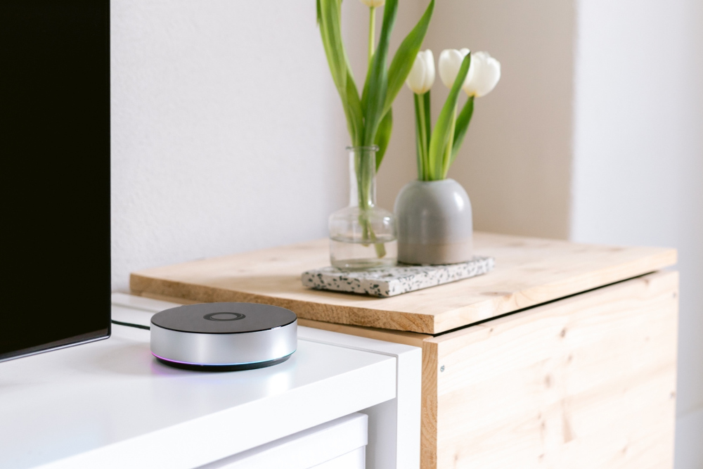 A smart home hub on a white cabinet. Behind it, tulips in a vase and a wooden box.