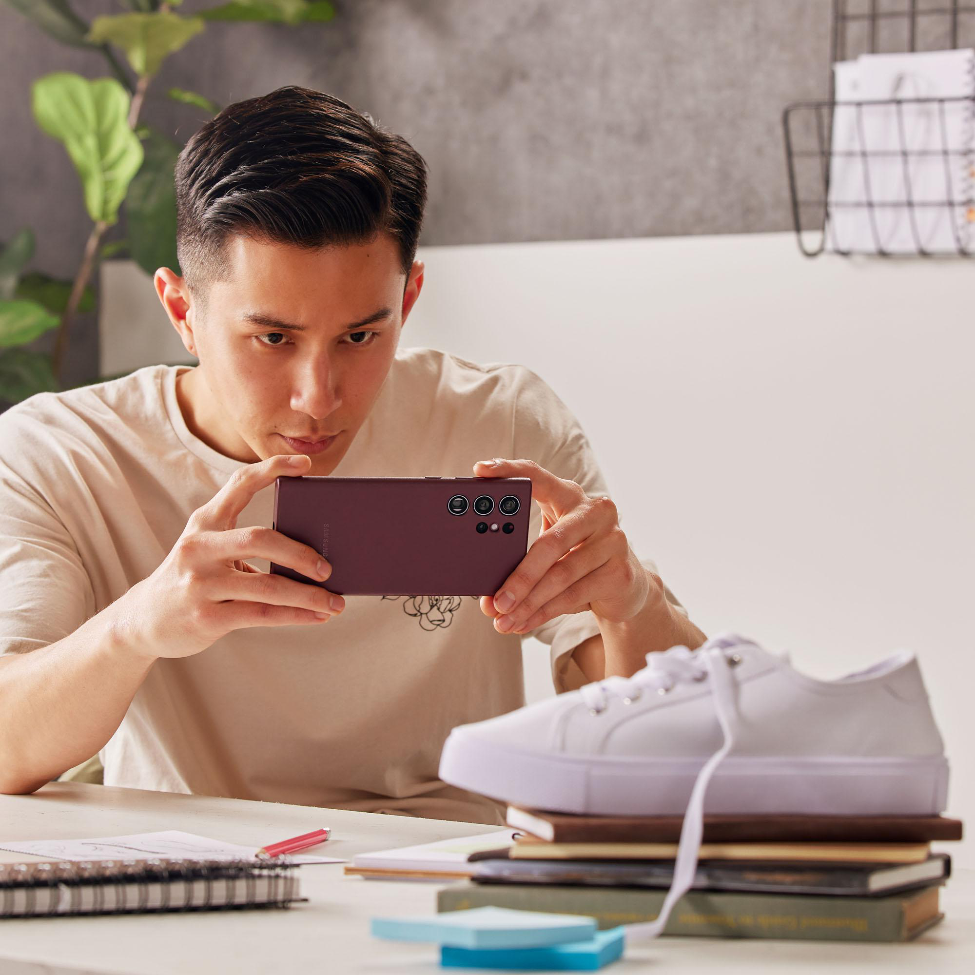 Ein Mann macht ein Foto mit einem lila Telefon, mit einem Schuh auf einem Bücherstapel.
