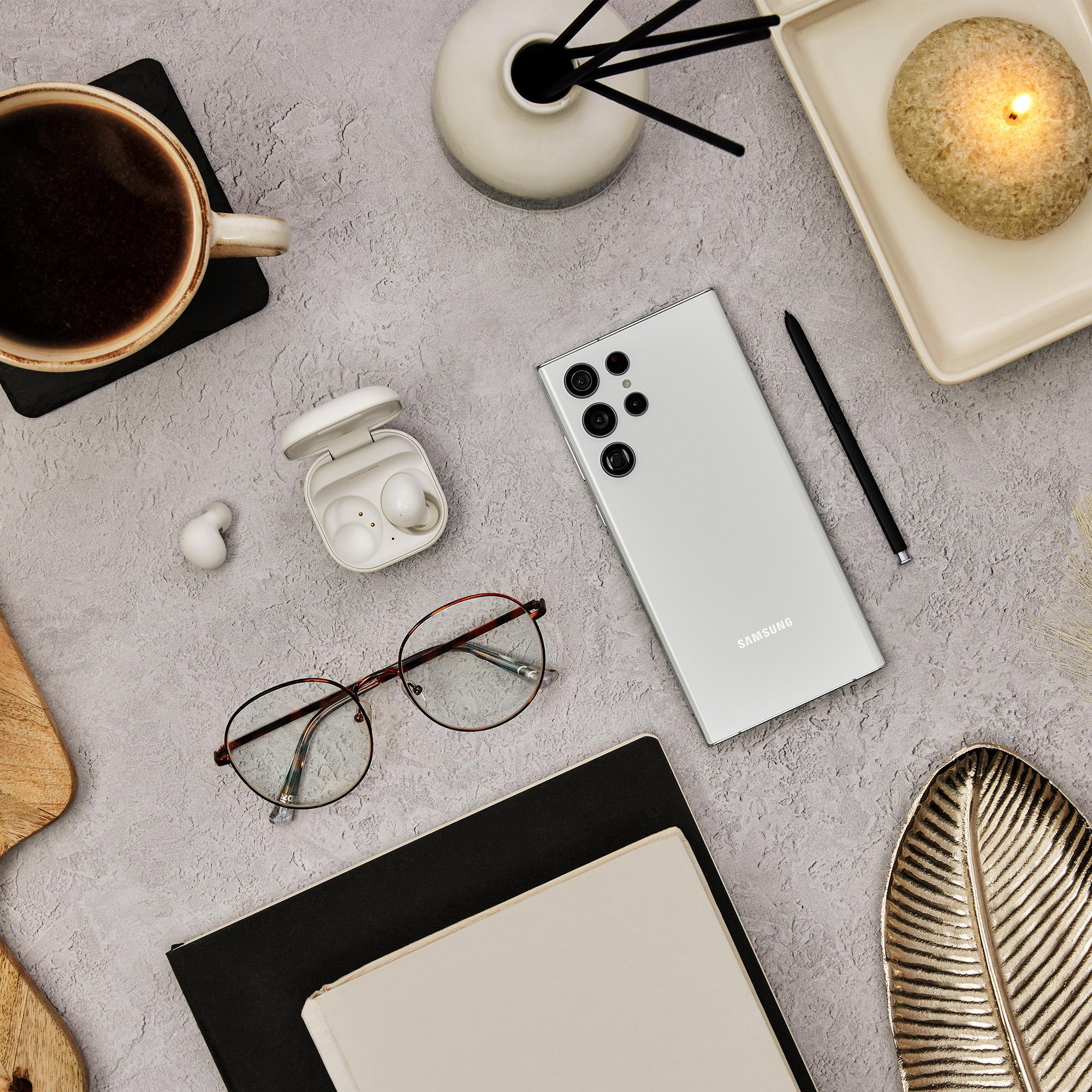 Draufsicht auf einen Schreibtisch mit Telefon, kabellosen Ohrhörern, Stift, Brille und anderen Gegenständen.