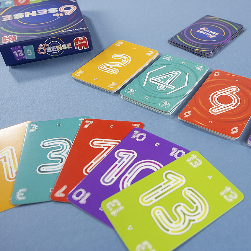 Nahaufnahme von 6th Sense Spielkarten, nummeriert 1-13, auf einer Oberfläche verteilt, mit Box.