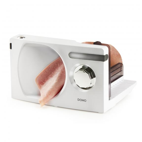 White meat slicer with a piece of meat. The slicer has a dial and a tray.