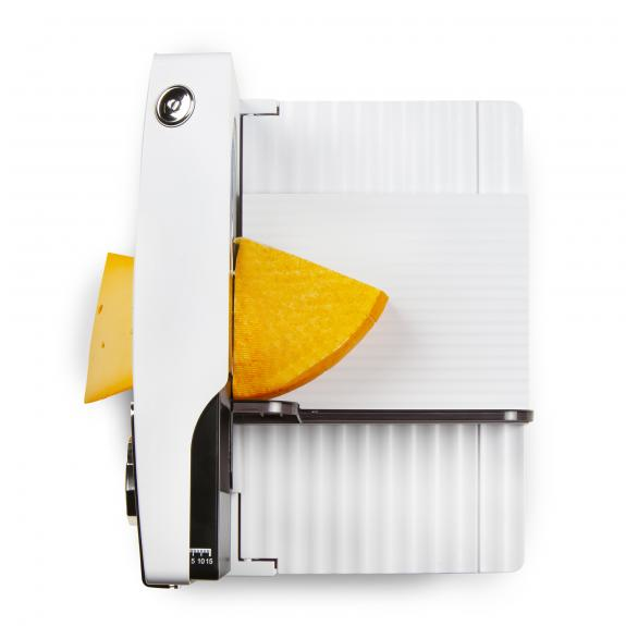 Cheese slicer with cheese. It has a white body and a metal blade. Cheese is yellow.