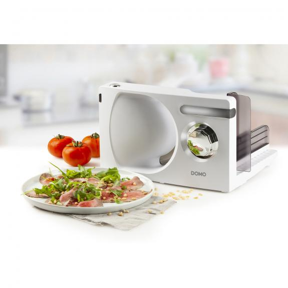 White food slicer with tomatoes and a plate of food in front of it.