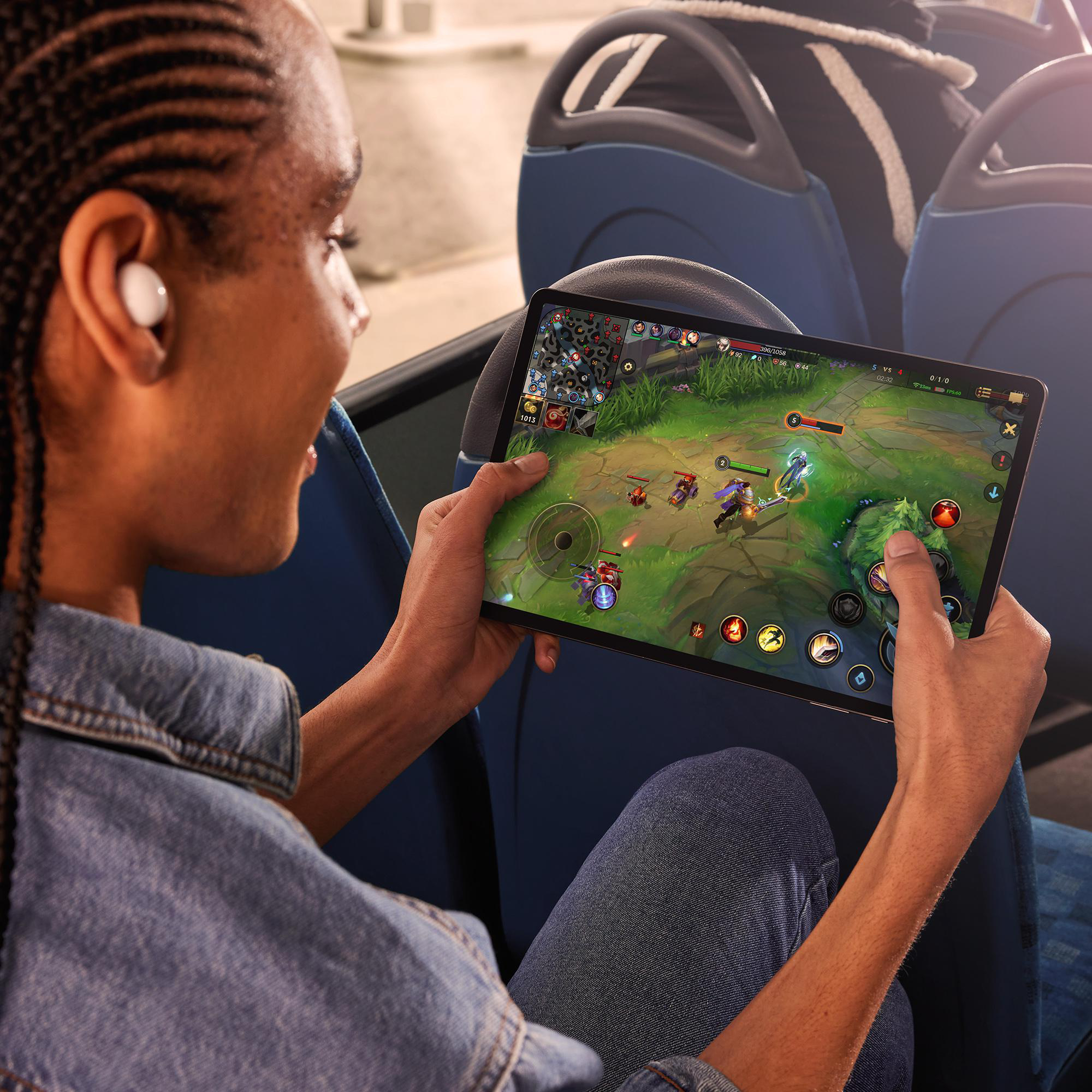 Eine Person spielt ein Videospiel auf einem Tablet. Sie tragen weiße Ohrhörer und lächeln.