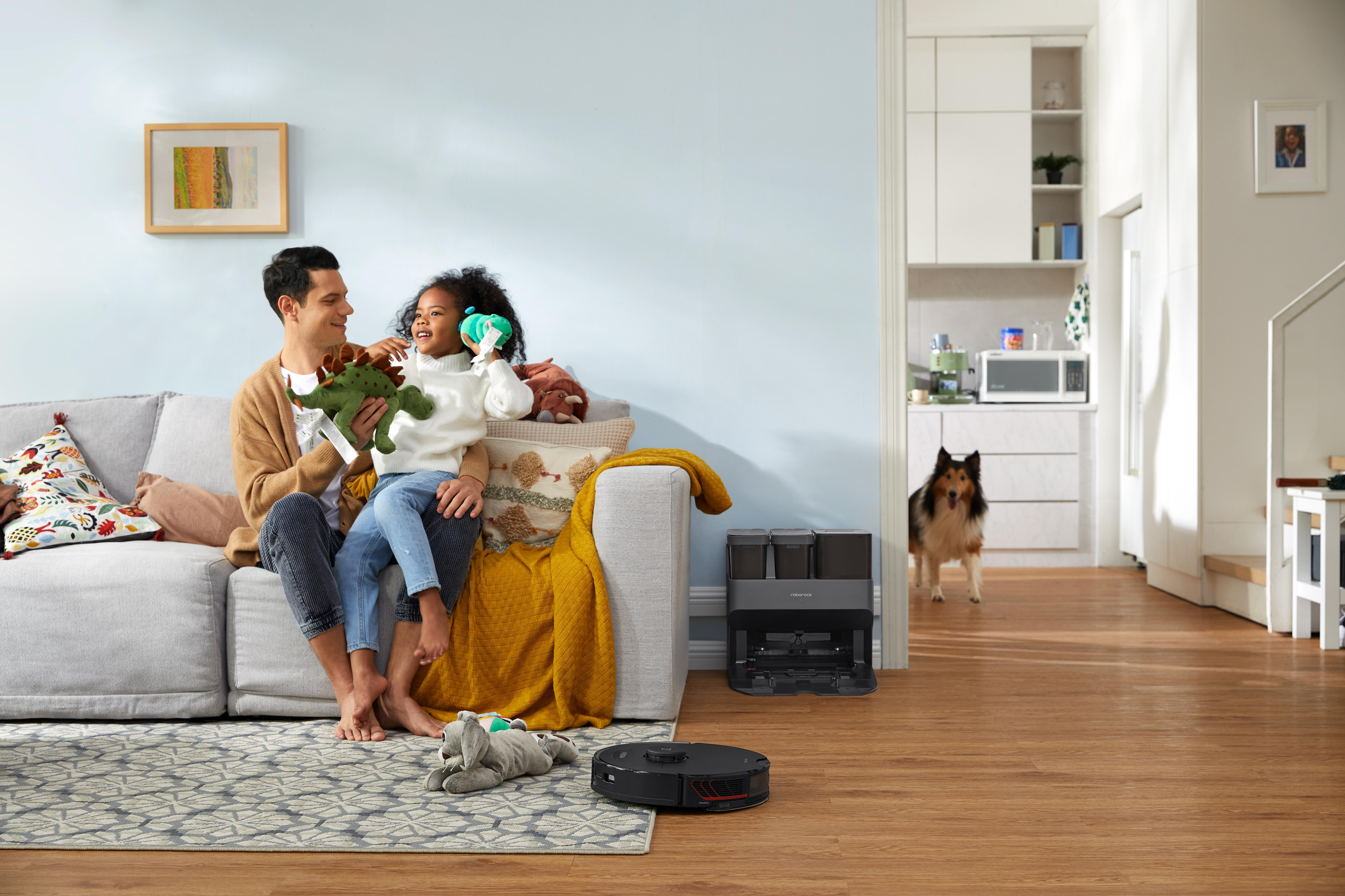 Eine Familie im Wohnzimmer mit Hund. Ein Roboter-Staubsauger steht auf dem Boden.