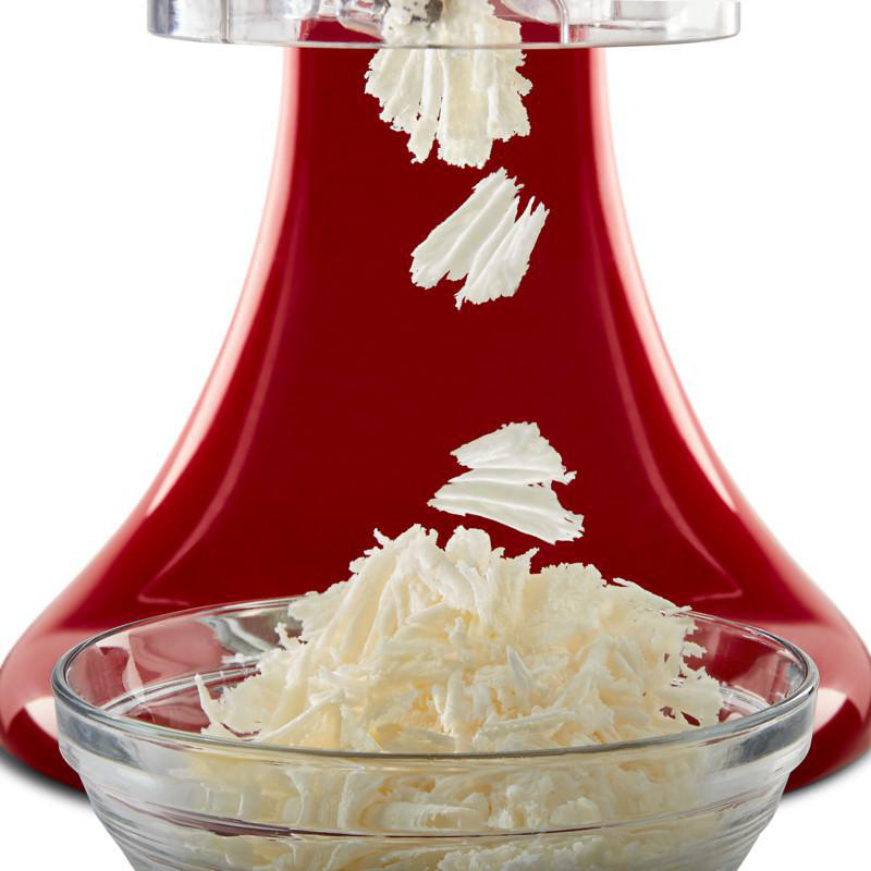Rote Küchenmaschine mit Käse, der in eine Glasschüssel fällt.