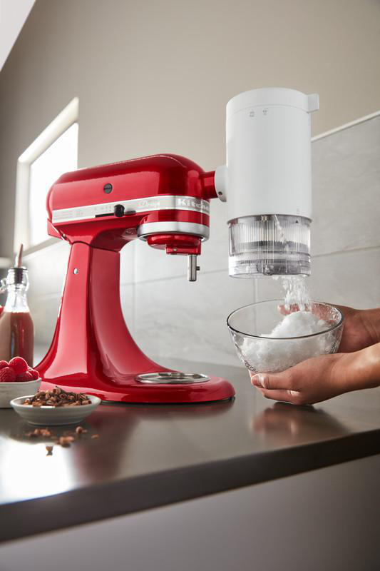 Roter Küchenmixer mit Eisrasierer-Aufsatz, mit Eis, das in eine Schüssel gerieben wird.