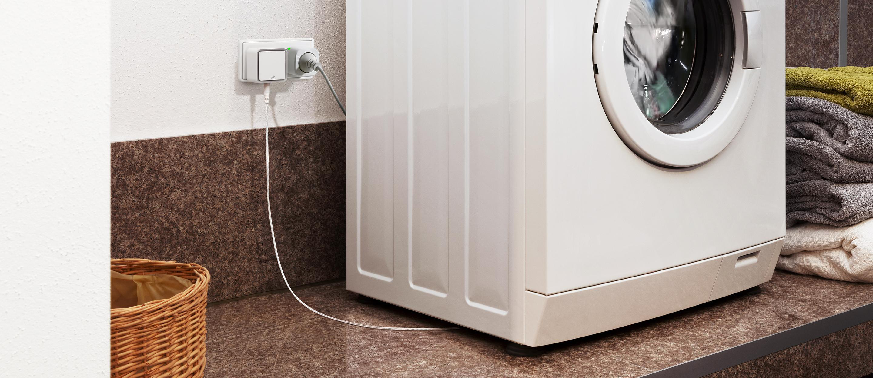 Weiße Waschmaschine in der Nähe einer Wand mit Steckdose. Ein Korb befindet sich im Vordergrund.