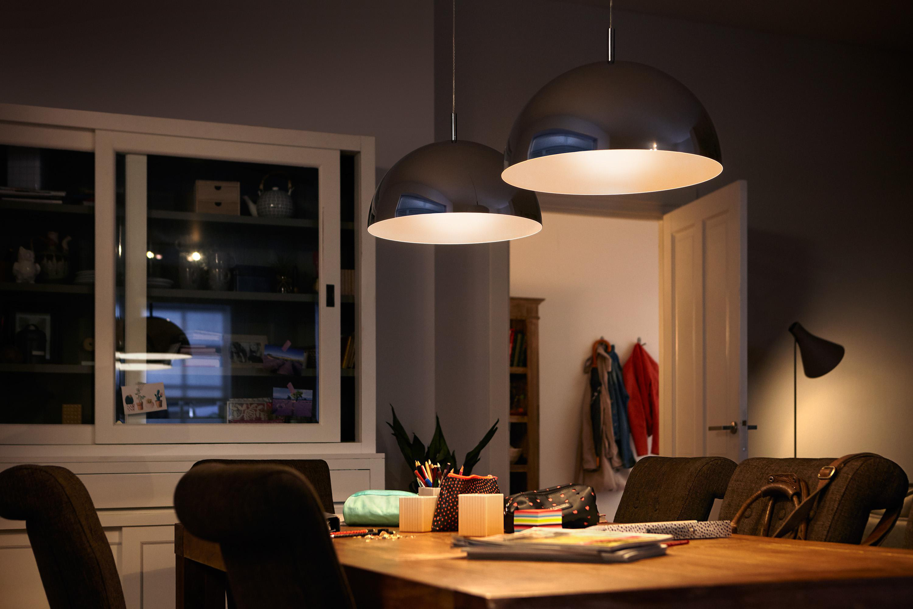 Ein Esszimmer mit Pendelleuchten über einem Tisch. Ein Türrahmen führt in einen beleuchteten Raum.
