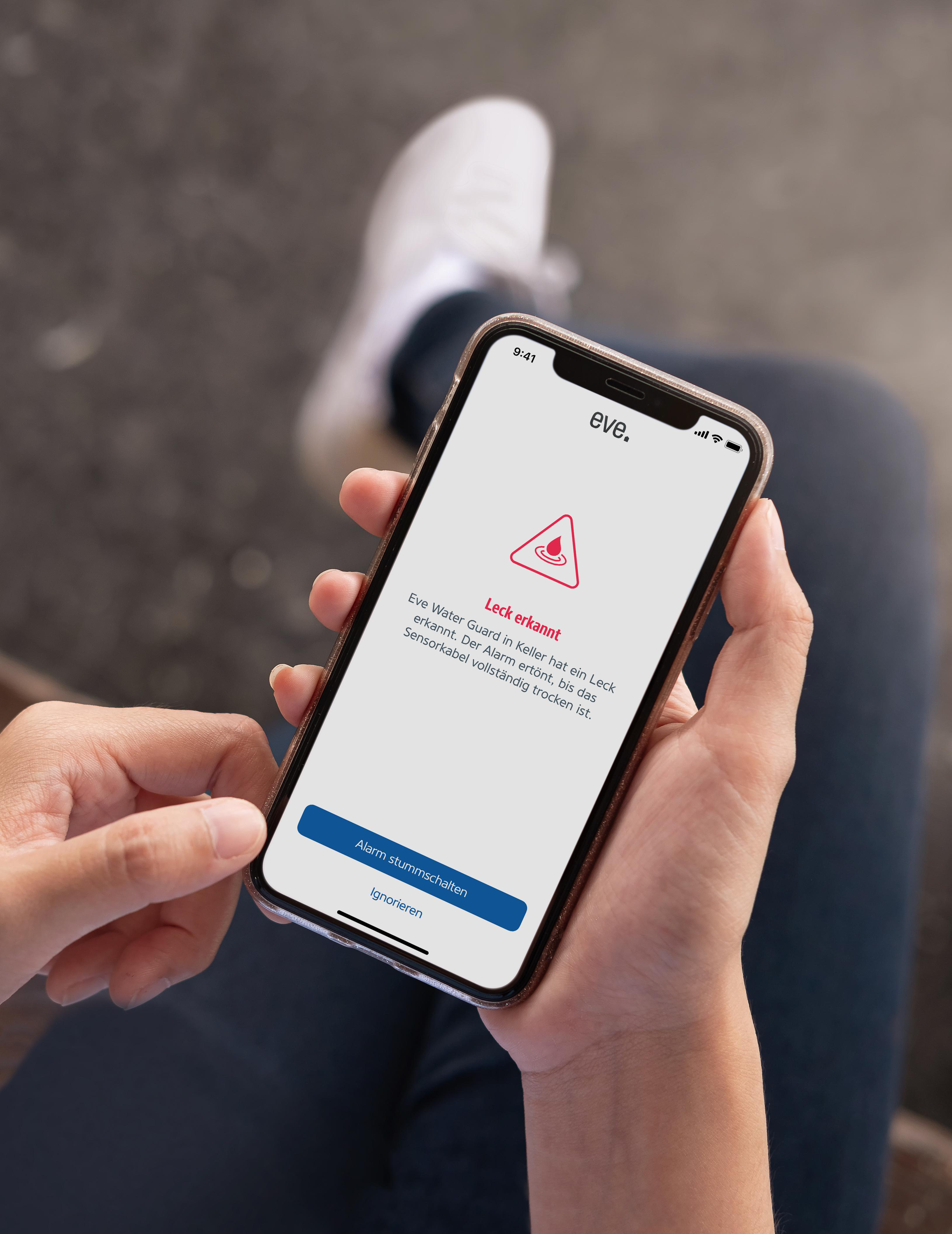 Person hält Smartphone mit Wasseraustritts-Alarm von der Eve-App.