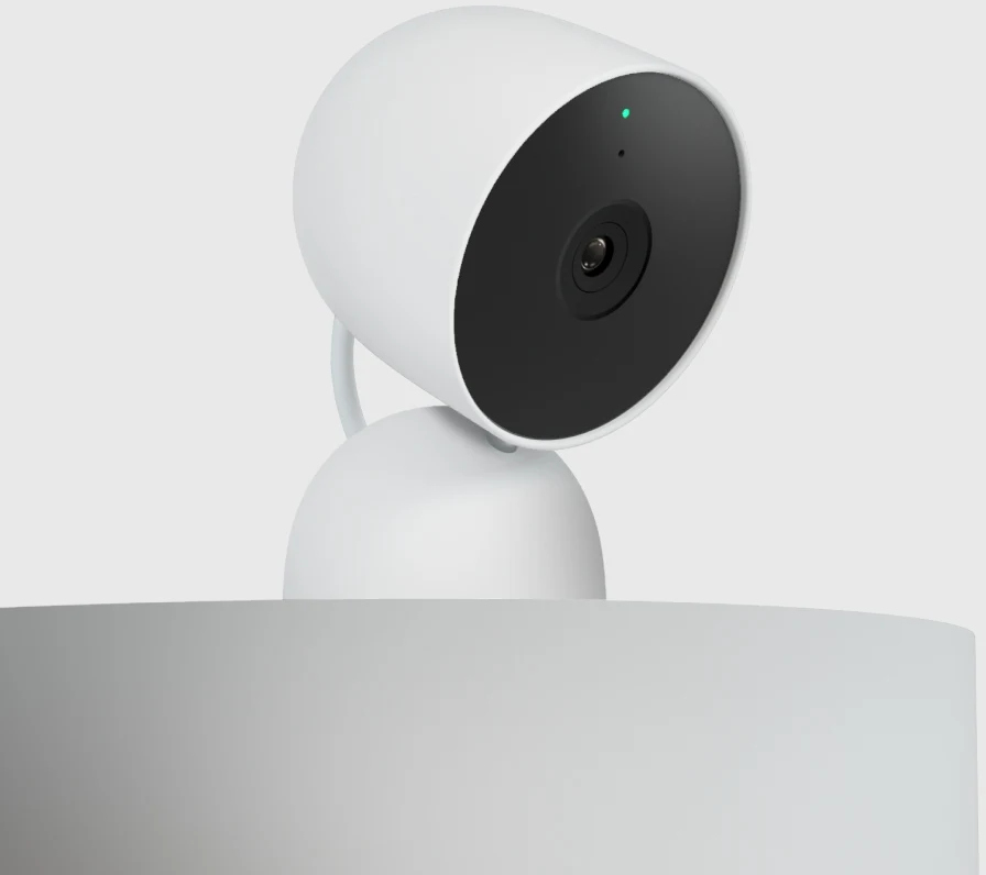 Caméra de sécurité blanche sur socle blanc, objectif noir, lumière verte.