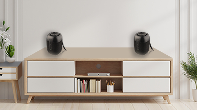 Zwei schwarze Lautsprecher auf einem Holzschrank vor einer weißen Wand. Die Lautsprecher sind zylindrisch.