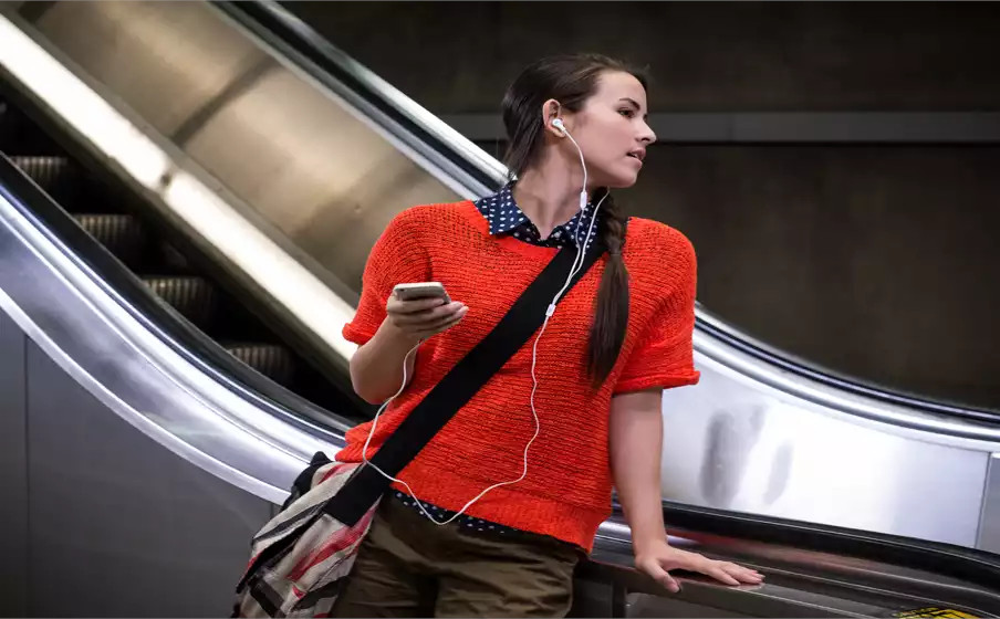 Vrouw op een roltrap met telefoon en koptelefoon, draagt rood.