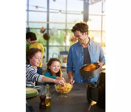 Family cooking with an air fryer. A man and two children are in the kitchen, smiling.